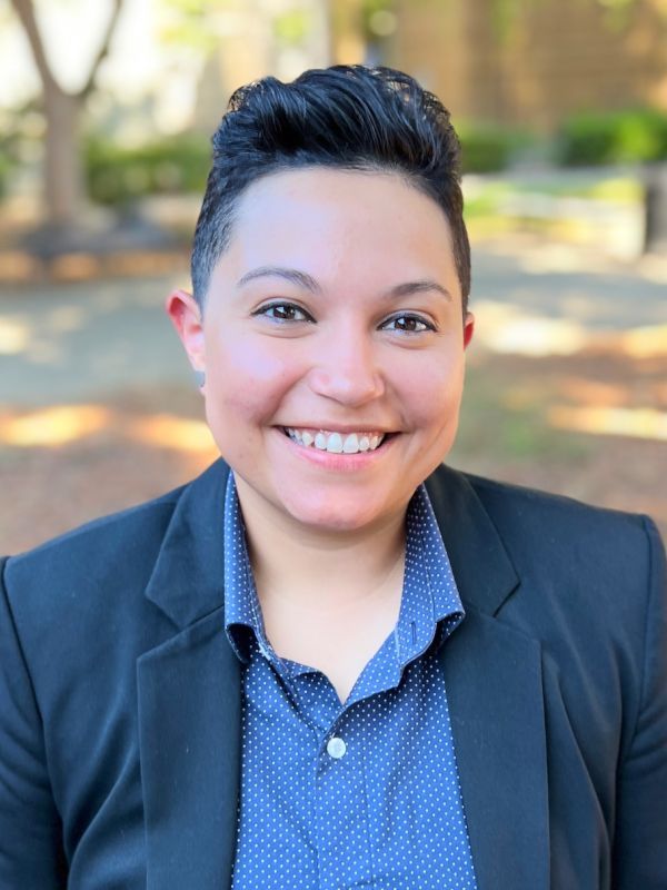 The smiling face of Halide Porras is pictured standing outside while wearing a light blue shirt and dark blue jacket.