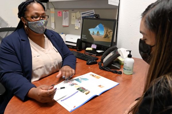 a woman at a desk shows a pamphlet to another woman