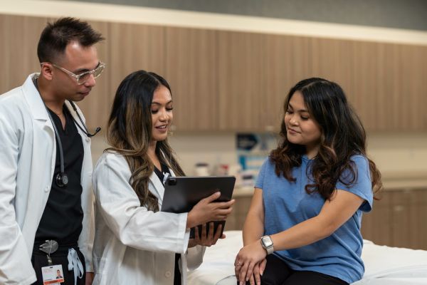 A man and a woman in white coats explaining contents of a tablet to a patient.