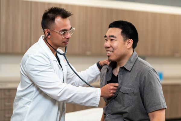 A doctor using a stethoscope to listen to the heartbeat of a male student.