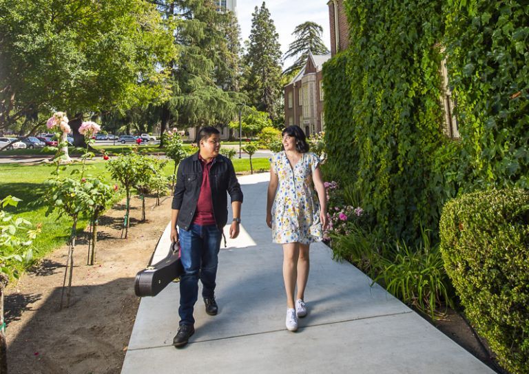 male student with cello case and female student walking under brick arch covered with ivy