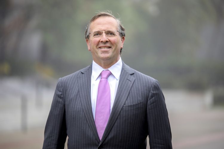 A portrait of Chris Micheli in a pinstripe suit and a pink tie.