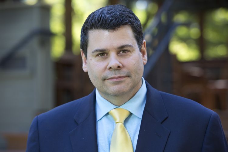 A portrait of Michael T. Colatrella Jr. in front of a background of greenery