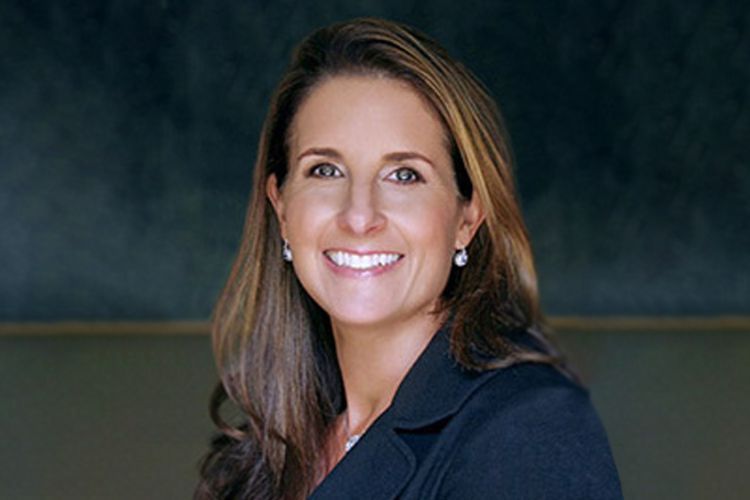 A headshot of a brunette woman in front of a blue background