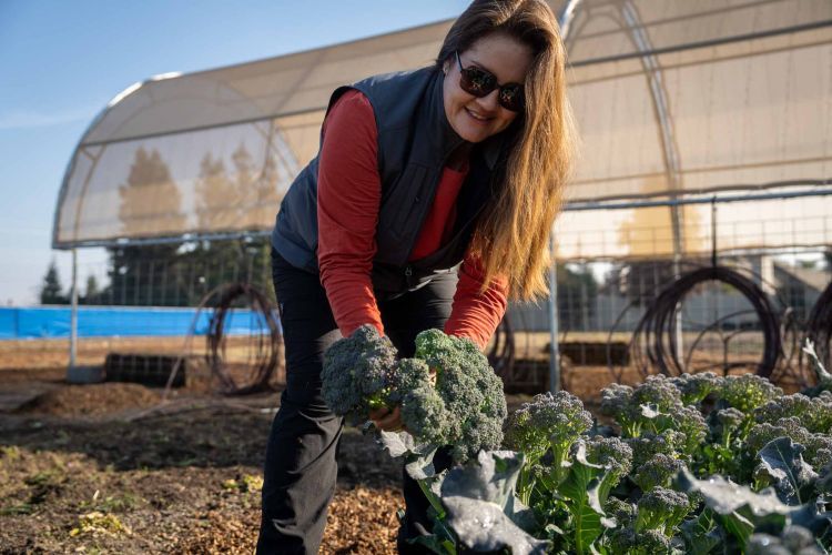 Jessica Coleman holds broccoli while standing in a garden