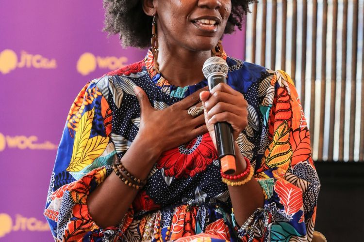 Sarah Webb sits on a stool holding a microphone