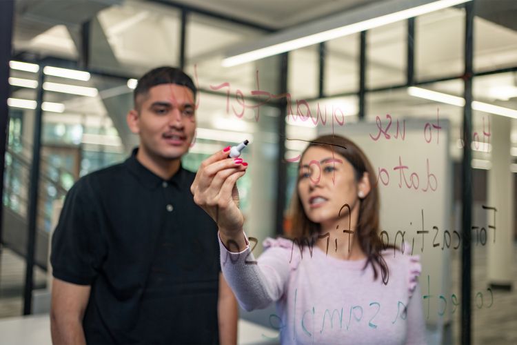 a professor and student look at an acrylic board as the professor writes on it