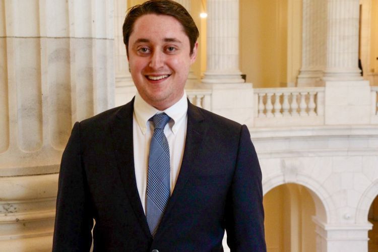 Man in black suit, blue tie, and white under shirt smiles for a headshot.