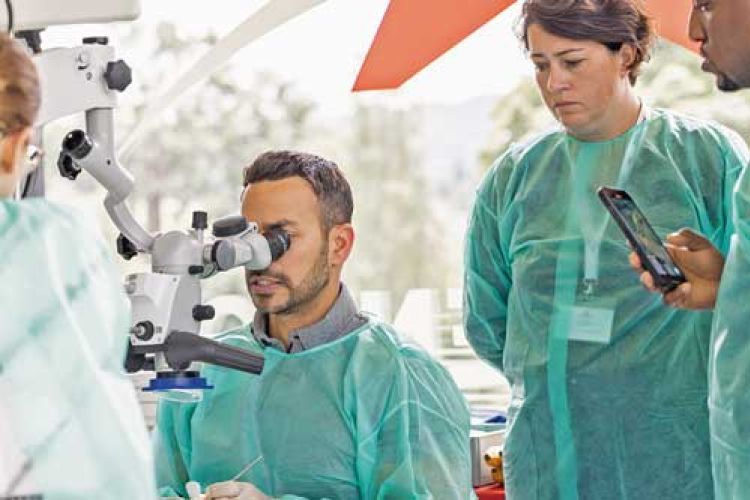 doctor looking into microscope with person behind him