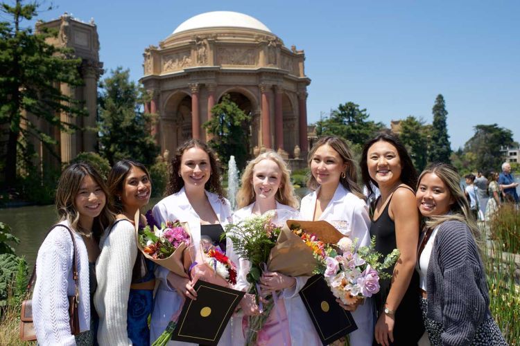 Smiling students wearing white coats in front of the Palace of Fine Arts