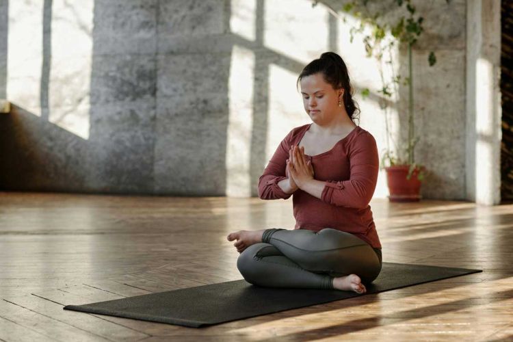 Woman with Down Syndrome holding a yoga pose. Photo by Cliff Booth: https://www.pexels.com/photo/photo-of-woman-meditating-alone-4056968/