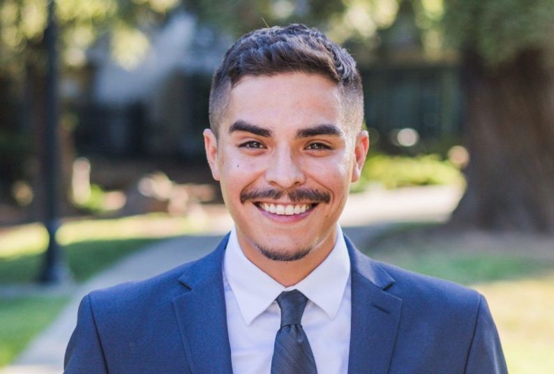 A man in a suit standing outside and smiling.