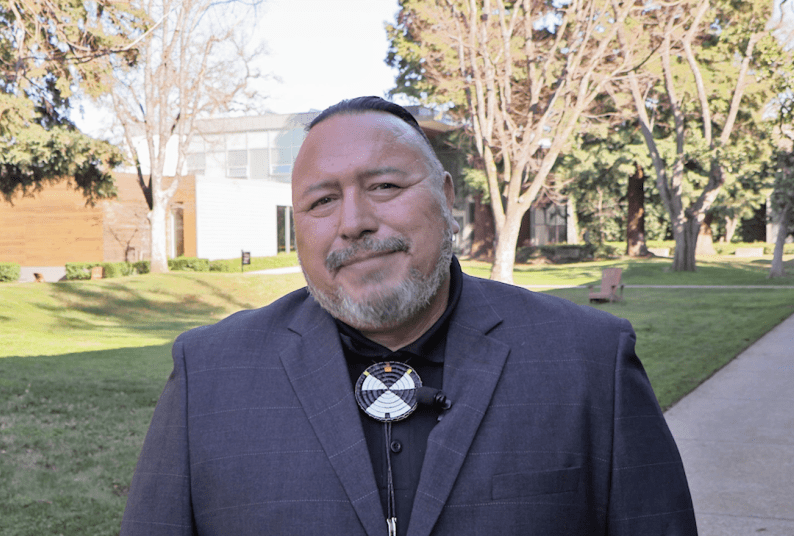 A man in a suit and bolo tie stands outside of the library building 