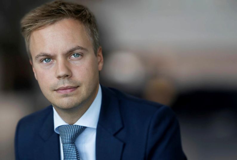 A man in a suit poses for a photo in front of a blurred background