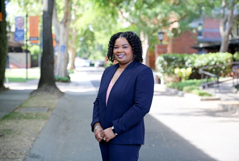 A woman in a navy suit poses outside smiling.