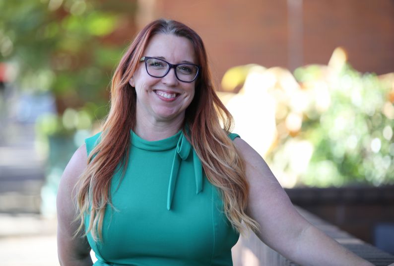 A red-haired woman in a green dress smiles for a photo while leaning on a railing 