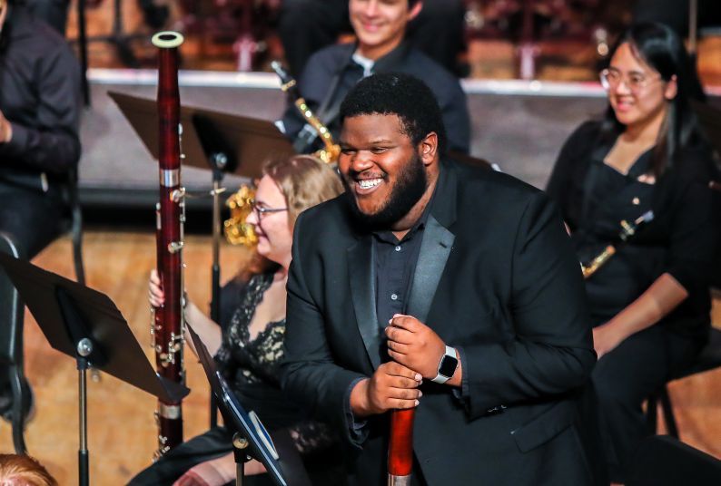 Three musicians smile as they stand on a stage.