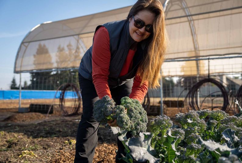 Jessica Coleman holds broccoli while working in a garden