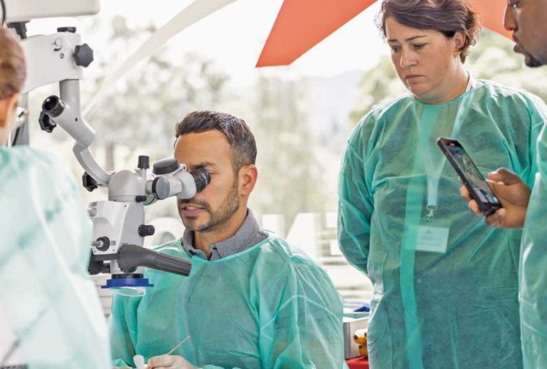 male doctor looking into microscope with person behind him