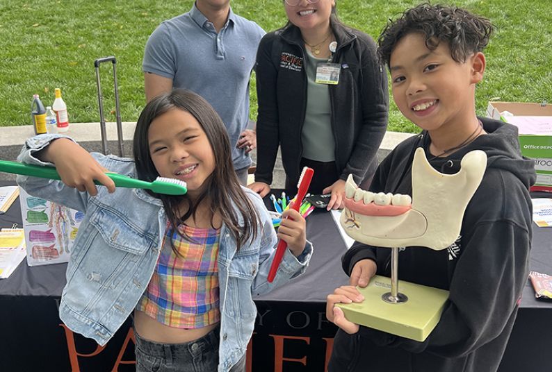 two children in front of two dental program student volunteers