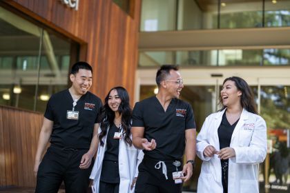 Four students are walking wearing scrubs and white coats