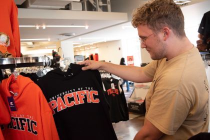 an alumni holds a black sweatshirt that reads University of the Pacific