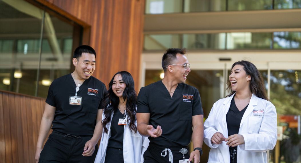 Photo shows four Nursing students at Pacific's School of Health Sciences talking and smiling while walking out of the nursing classroom.