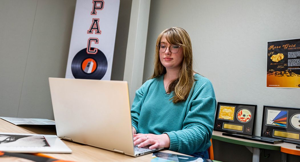 college student sitting at a desk with a laptop and vinyl albums