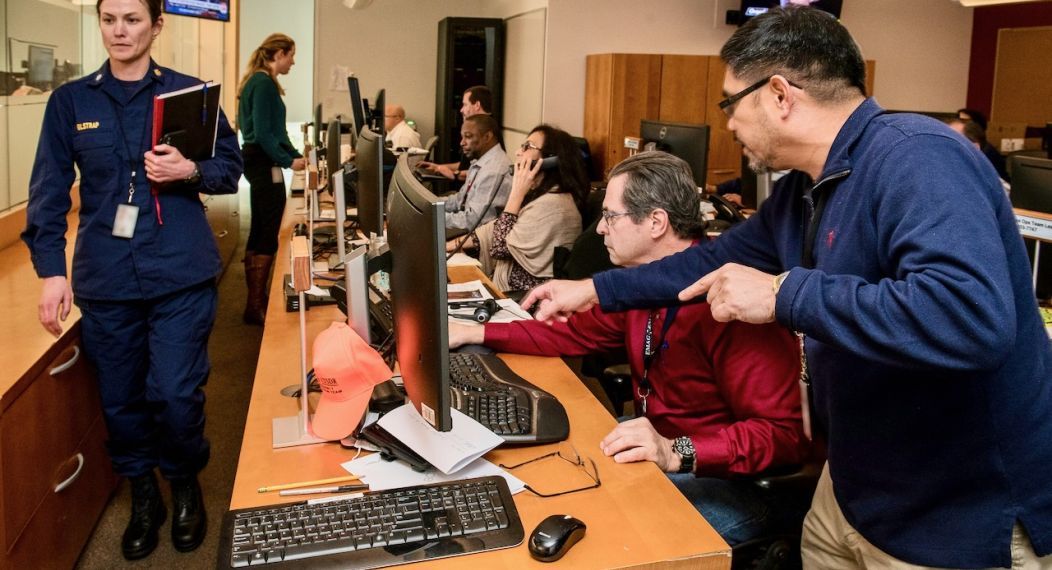 An emergency response team is shown working at their computer monitors.