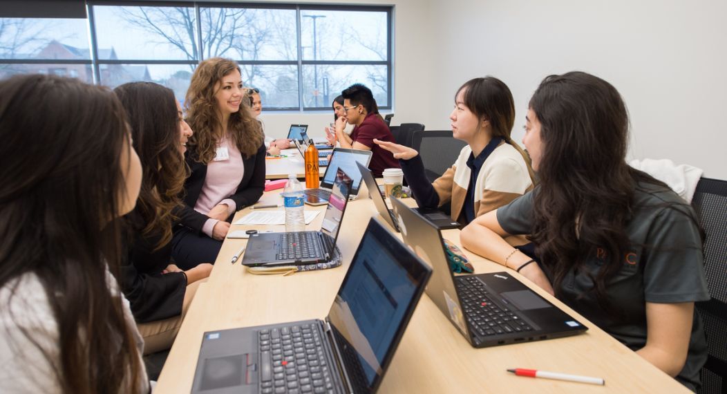 Photo shows 5 PA students sitting and talking in front of their laptops.  