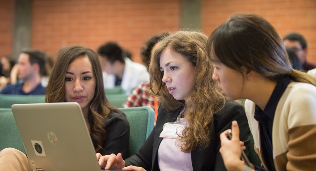 Photos shows three PA students at UOP gathered around a laptop in a lecture hall. 