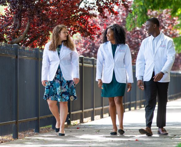 students in white coats walking on sidewalk