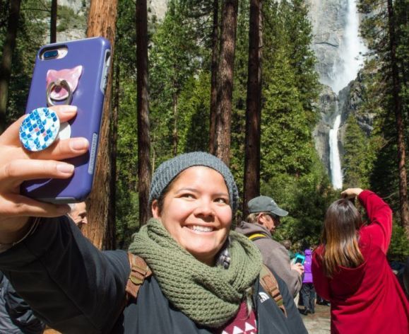 a student takes a selfie at a national park with a waterfall in the background