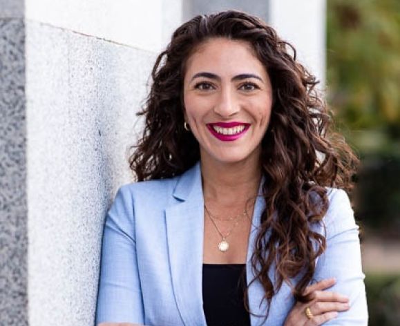 A woman wearing a suit smiles for a photo outside