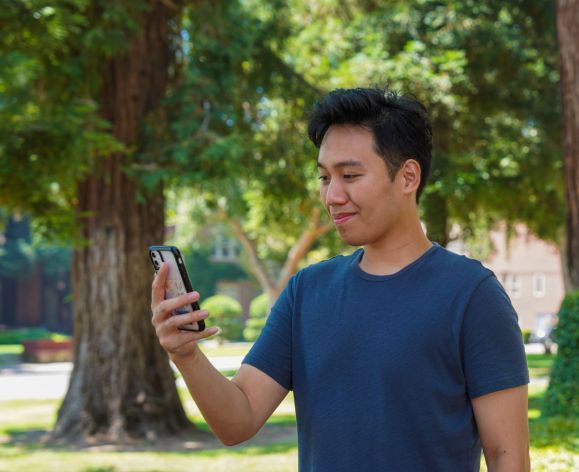 Image of male student looking down at phone and smiling.